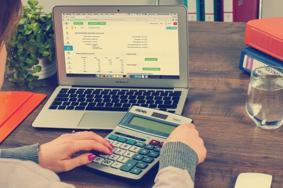 Pessoa conferindo planilha no notebook com uma calculadora